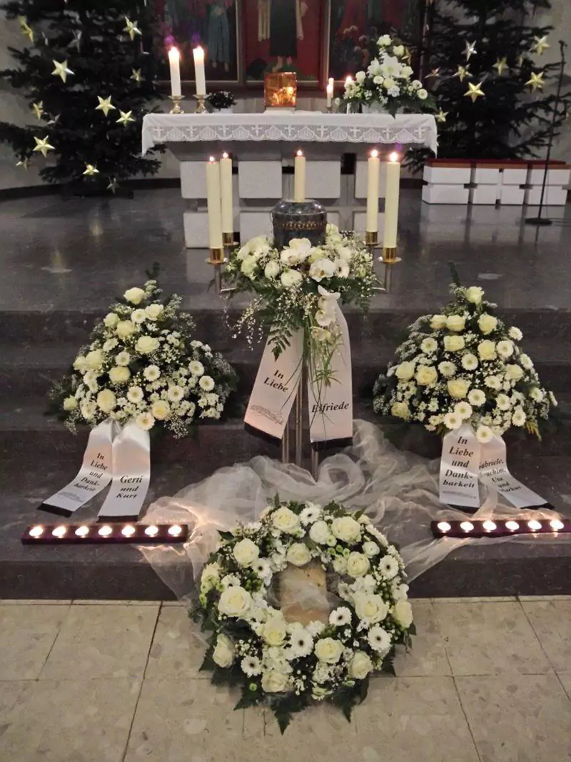 Urne, Kränze und Blumenschmuck vor einem Altar