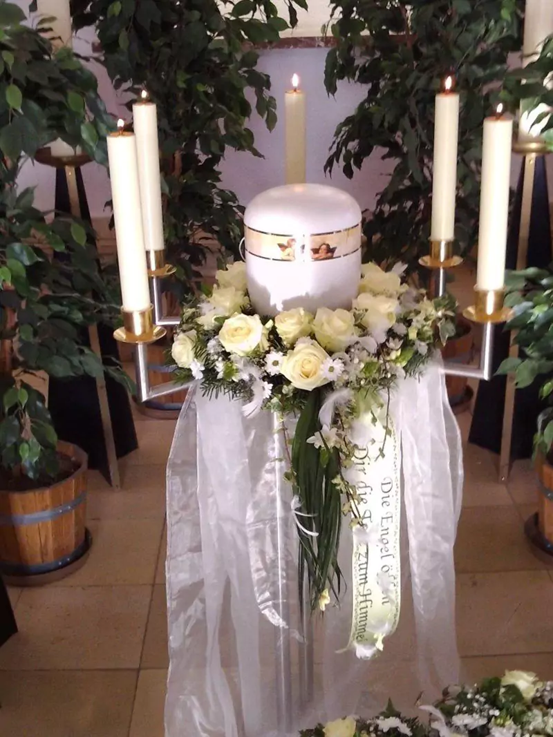 weiße Urne mit 5 weißen Kerzen und Blumenschmuck aus weißen Rosen