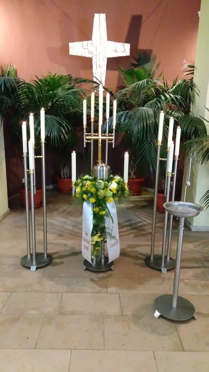 Urne mit Kerzen und Blumenschmuck mit einem Kreuz im Hintergrund