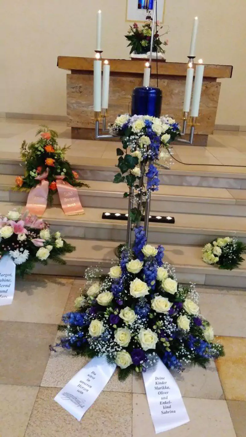 Urne mit blau-weißem Blumenschmuck vor einem Altar